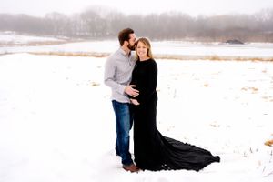 A winter maternity photo with a flowing black dress against a snowy landscape.