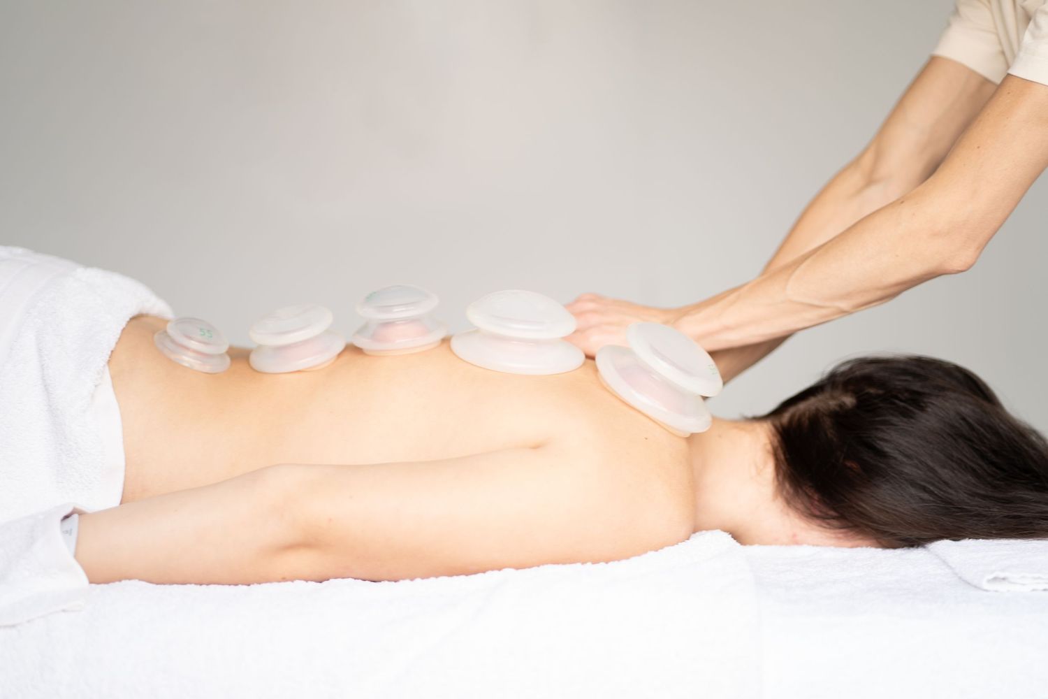 Hot stone massage therapy being performed on back with white stones.