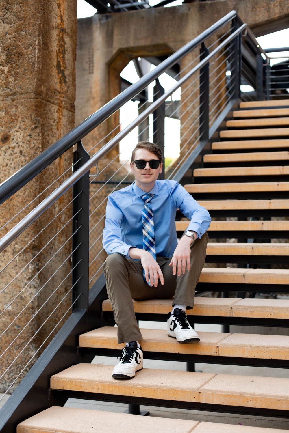 A person in business casual attire sits on wooden stairs with industrial metal railings.