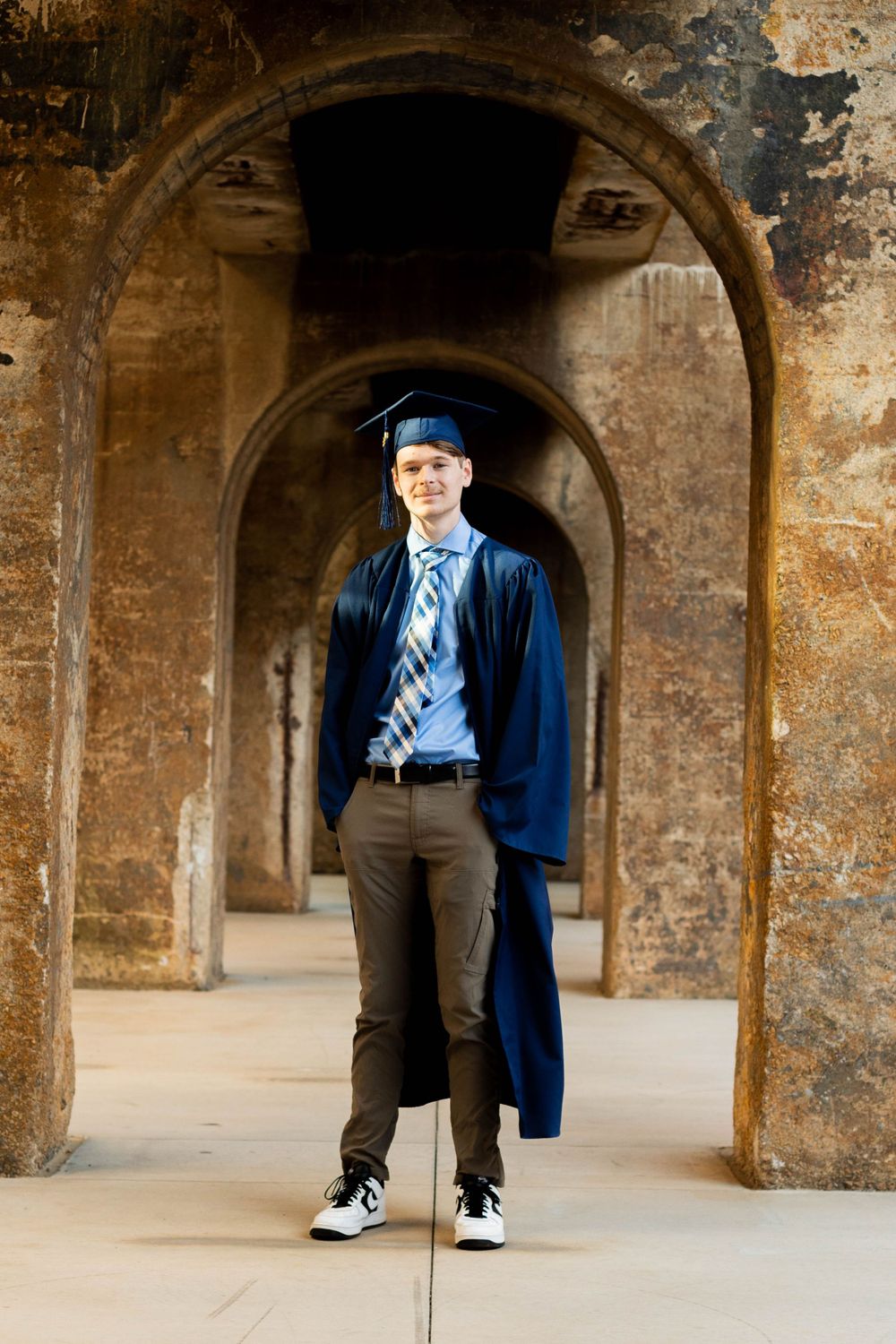 A graduate in cap and gown poses in a historic stone archway.