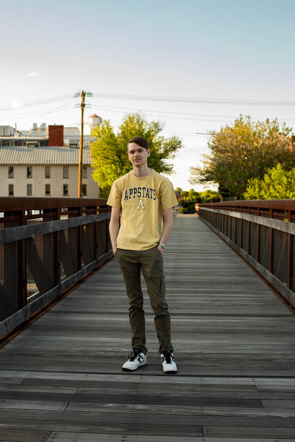 Person in yellow Appstate shirt and dark pants stands on wooden walkway.