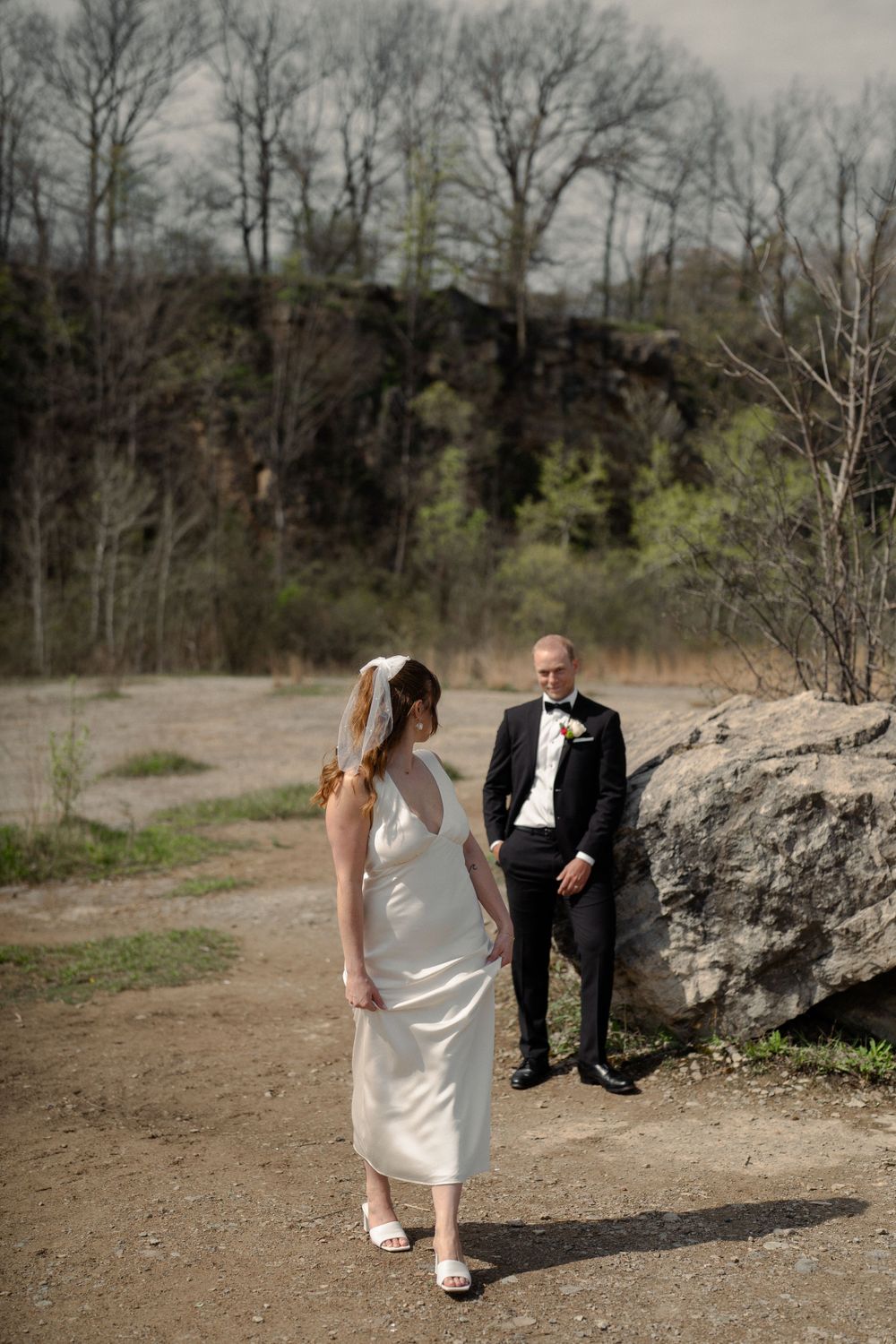Romantic outdoor wedding portrait against rocky terrain and bare winter trees.