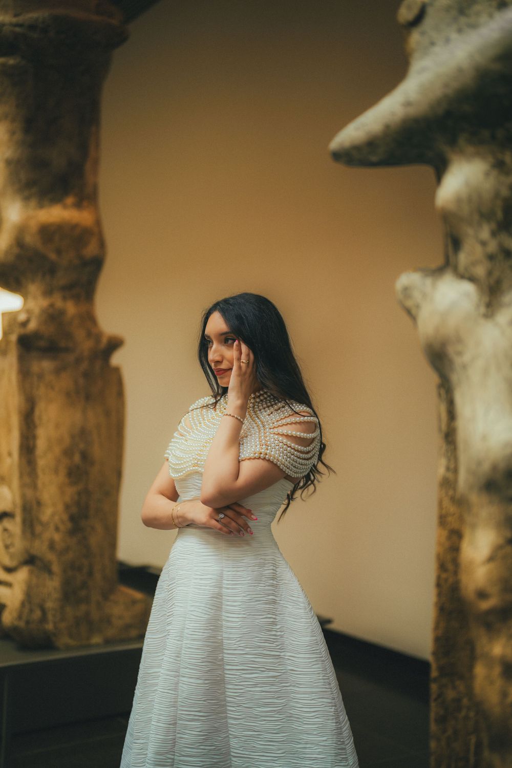 A dreamy fashion portrait of a woman in a flowing white dress standing between stone archways with moody lighting.