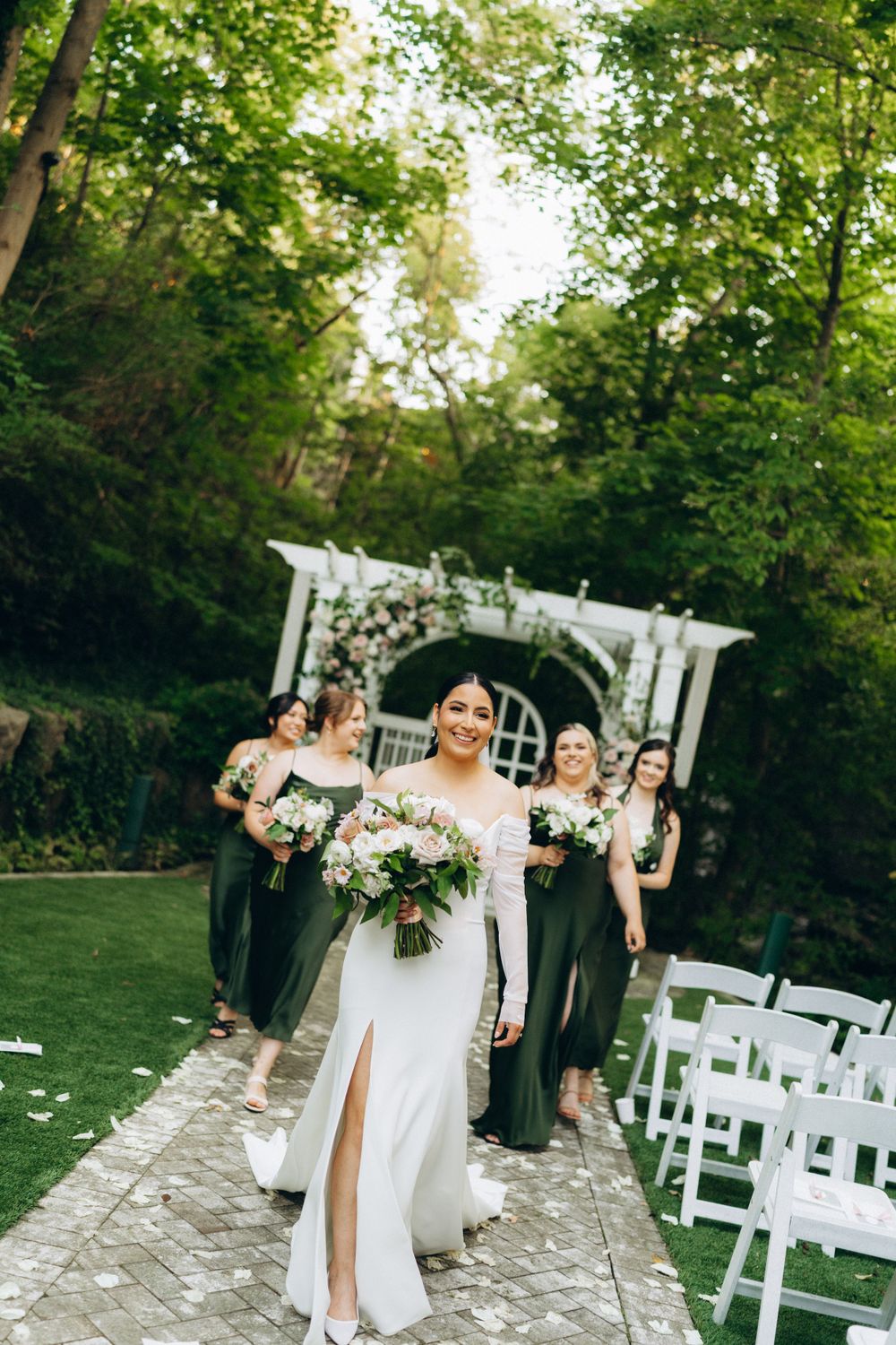 Wedding ceremony in a lush garden setting with a floral-adorned white pergola archway.