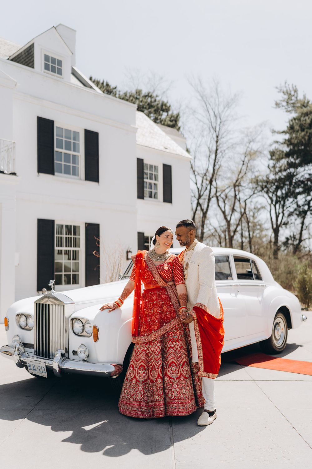 Traditional South Asian wedding couple pose with vintage white Rolls Royce in front of colonial style mansion.