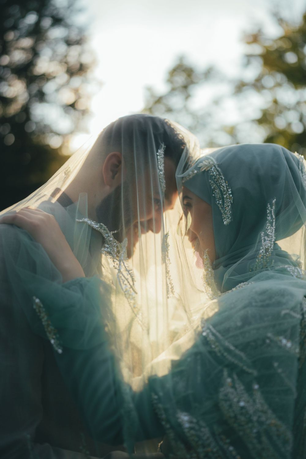 Sunlit intimate moment between two people in veils during wedding ceremony outdoors.