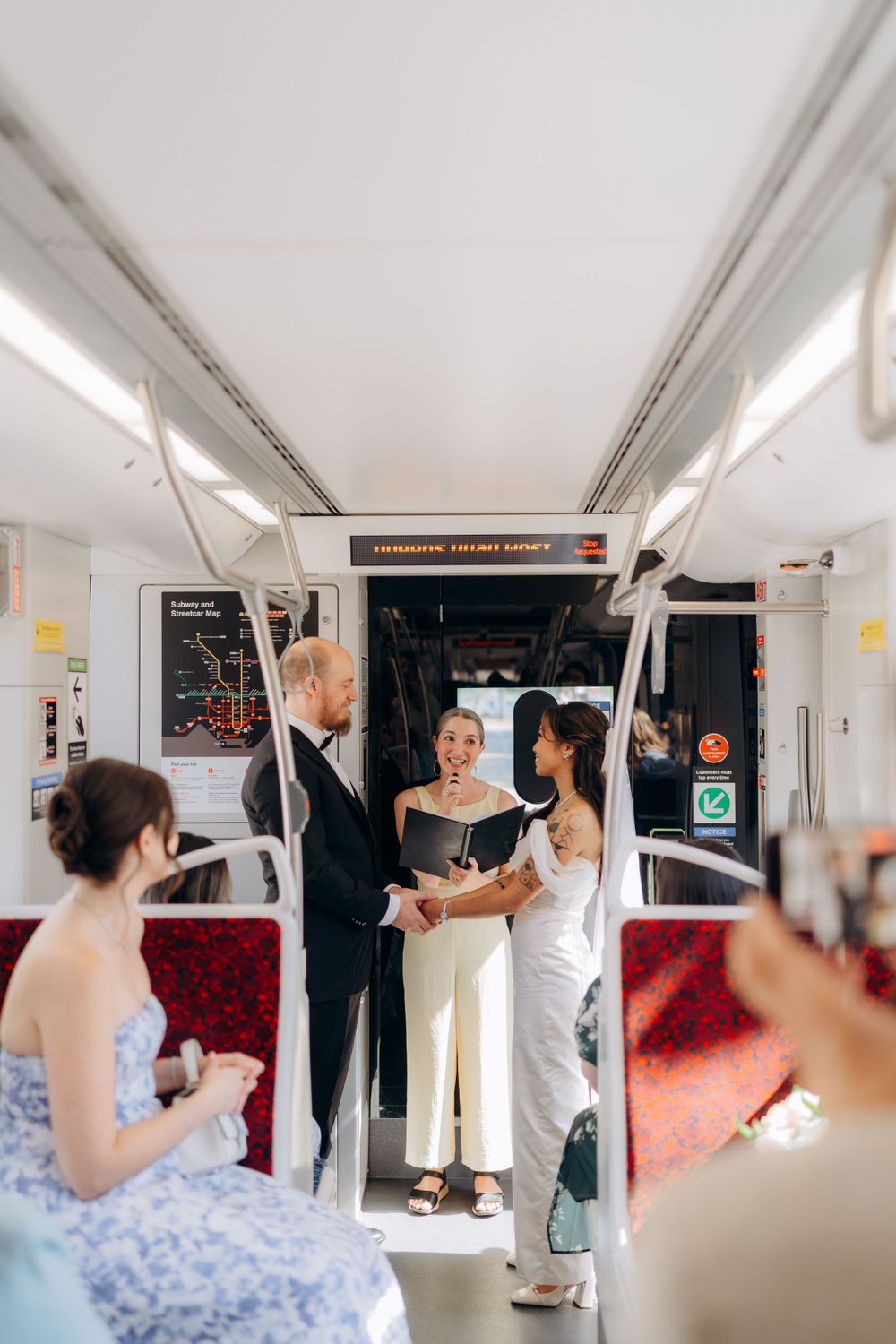 A wedding ceremony takes place inside a moving subway car with people gathered around in formal attire.