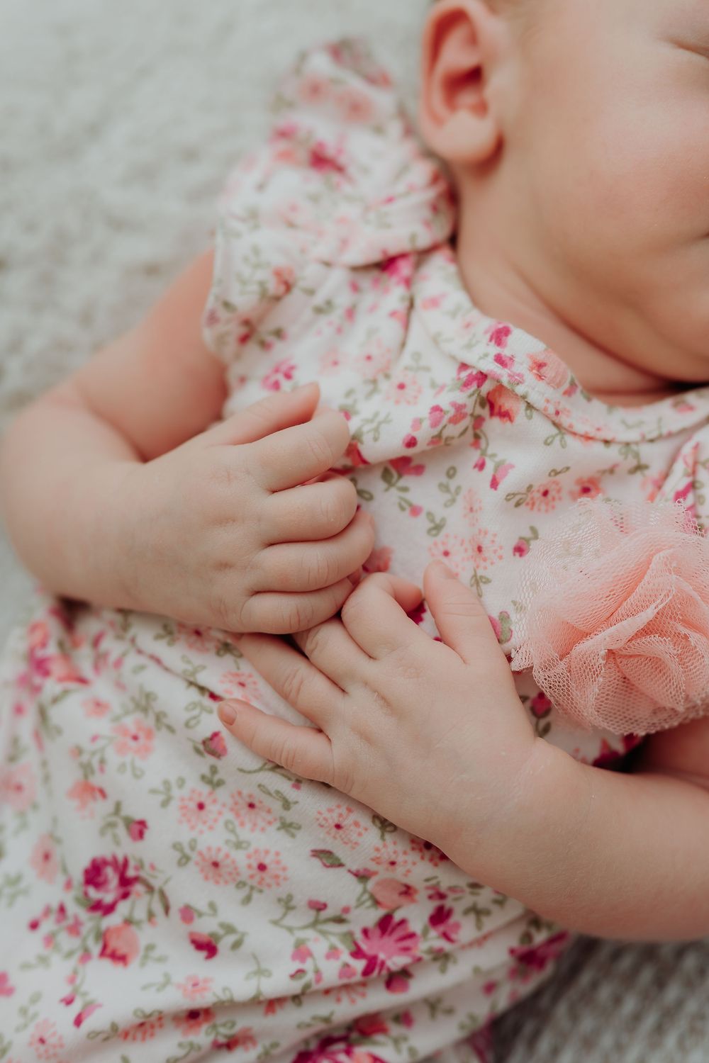 Close-up photo of tiny baby hands resting on delicate pink and white floral fabric.
