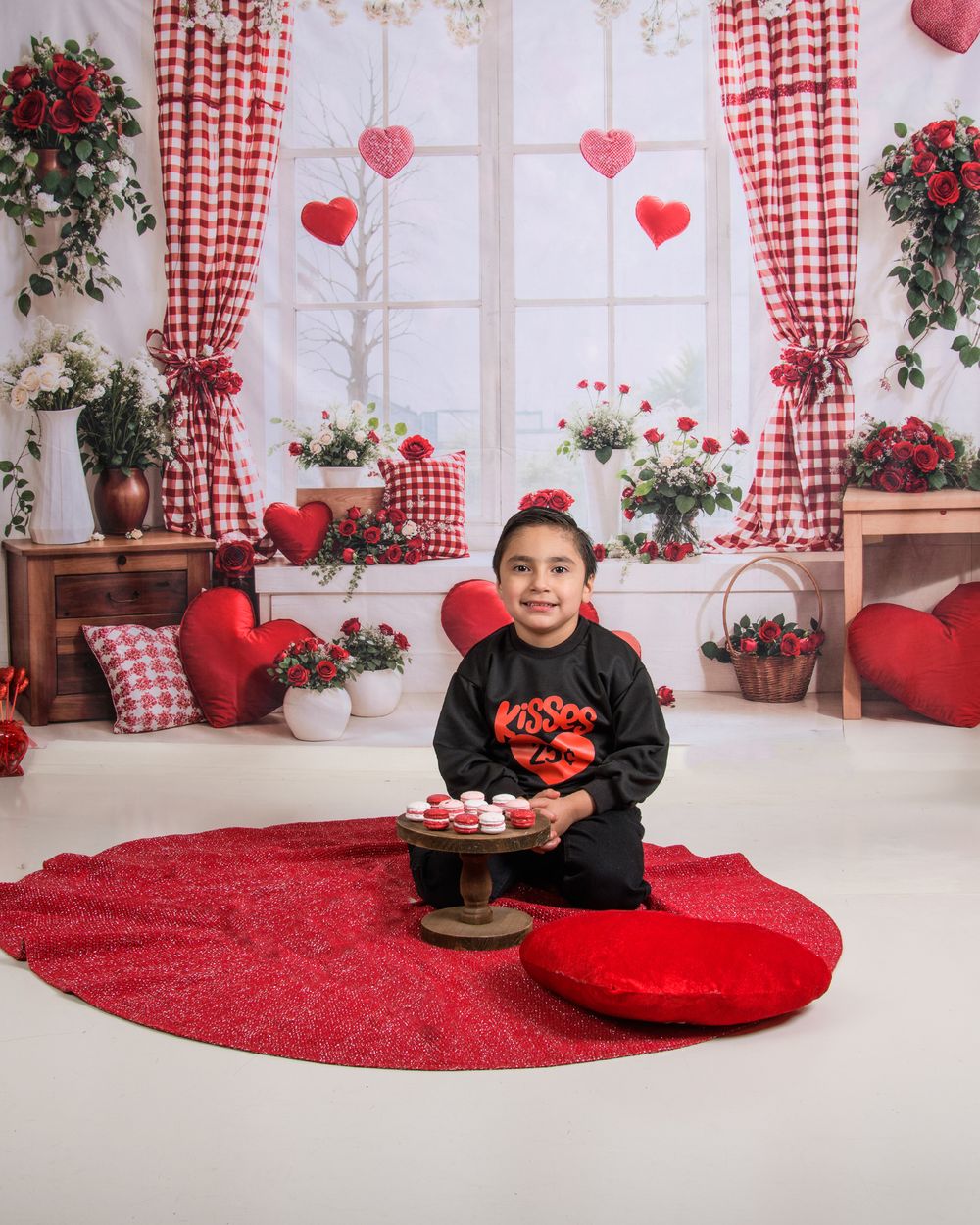 Valentine's Day themed photo setup with red and white gingham curtains, heart decorations, and roses in a cozy interior.