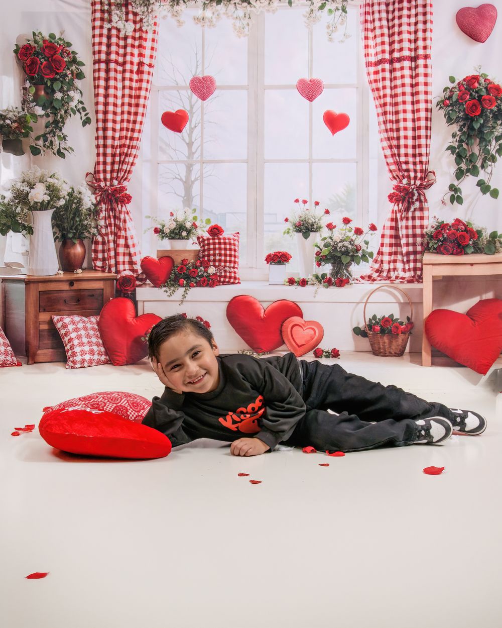 Romantic Valentine's day setting with red hearts, gingham curtains, and scattered rose petals in a cozy white room.