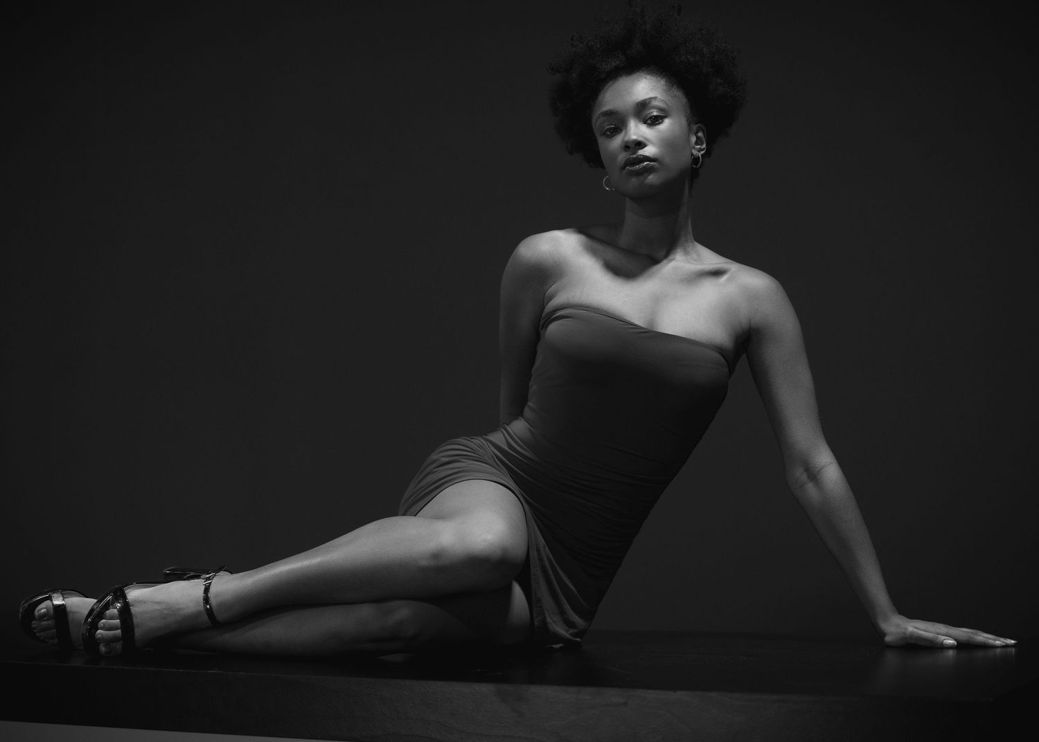 A gorge brown skin model with a red dress on a black table with a black background.