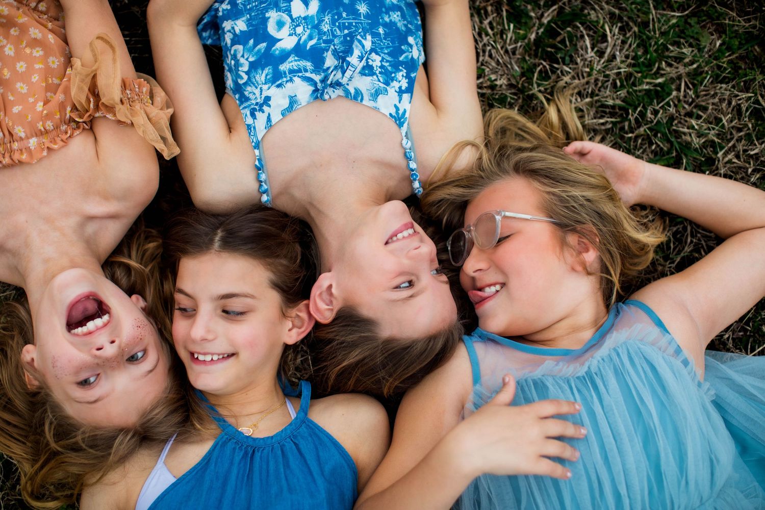 Friends lying in grass wearing blue dresses share joyful laughter together.