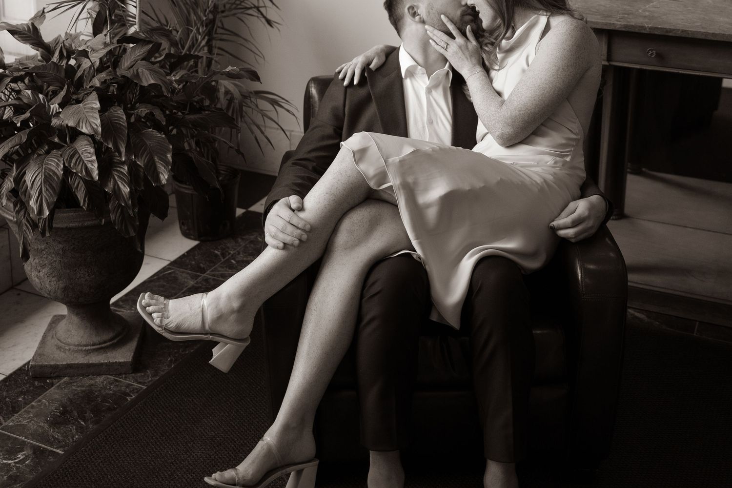 A romantic black and white photo of a couple seated intimately on a sofa with elegant formal attire.