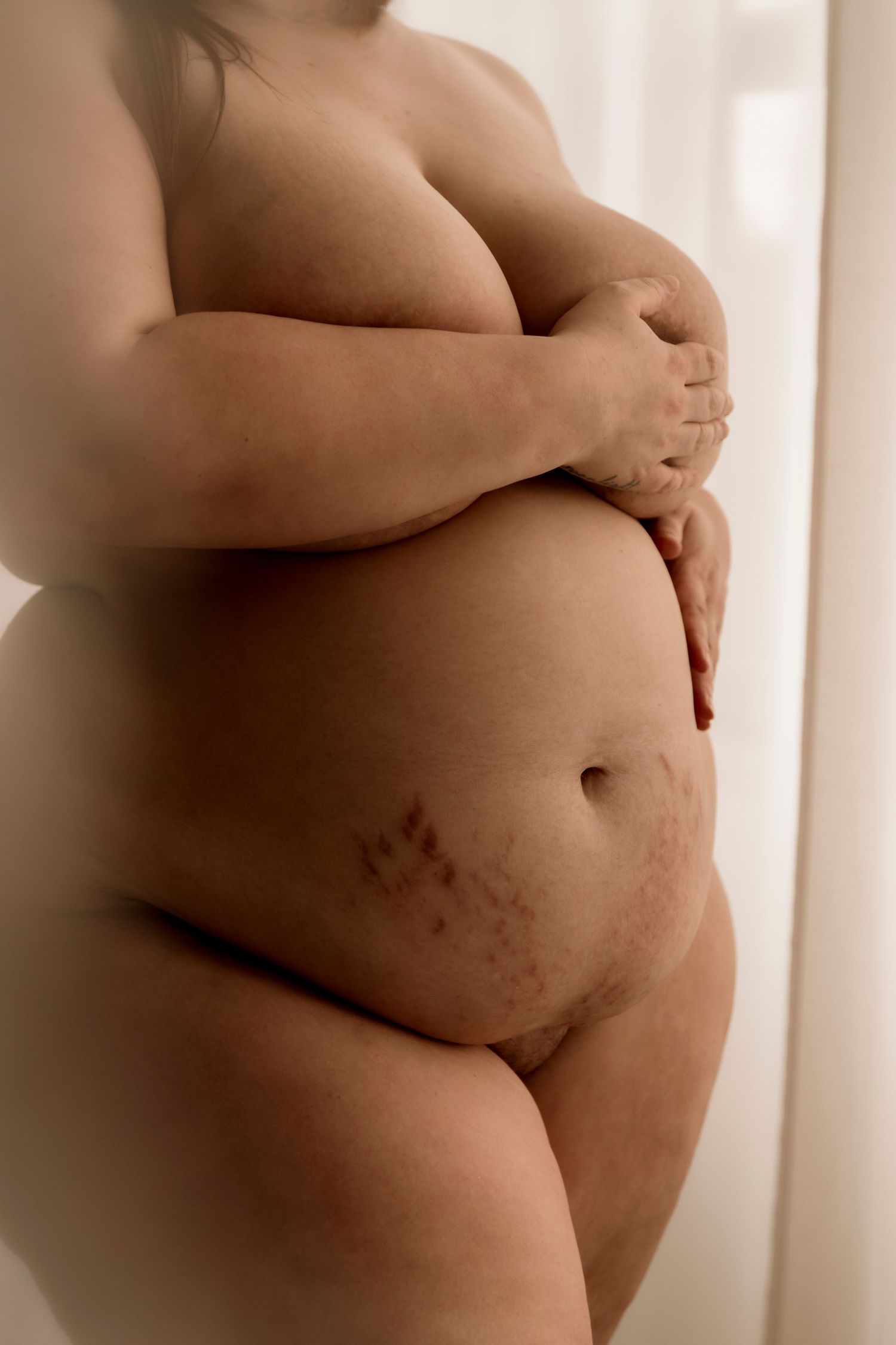 An artistic sepia toned photograph showing stretch marks on a pregnant woman's belly emphasizing natural beauty and motherhood.