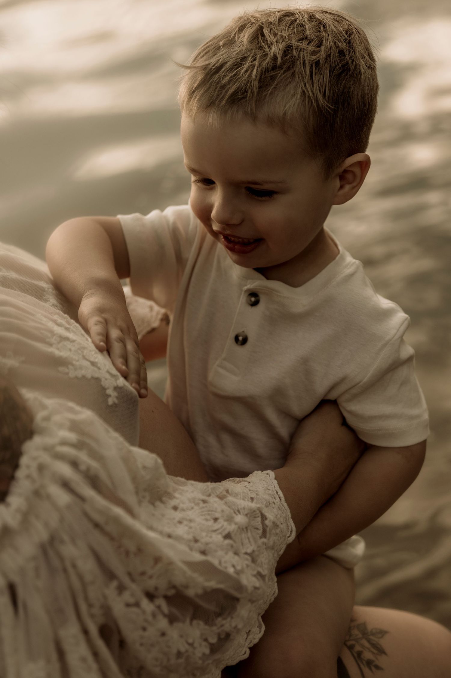 Young child in white polo shirt playing with lace fabric in a warm sepia-toned portrait.