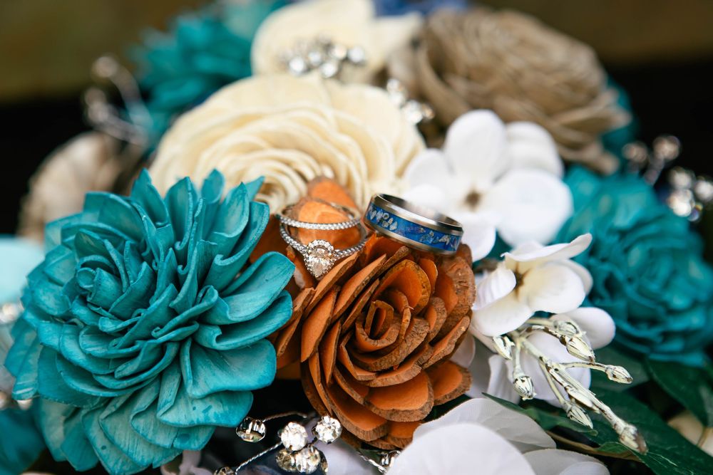 Wedding bouquet with teal and brown satin flowers accented with white blossoms and a blue ring detail.