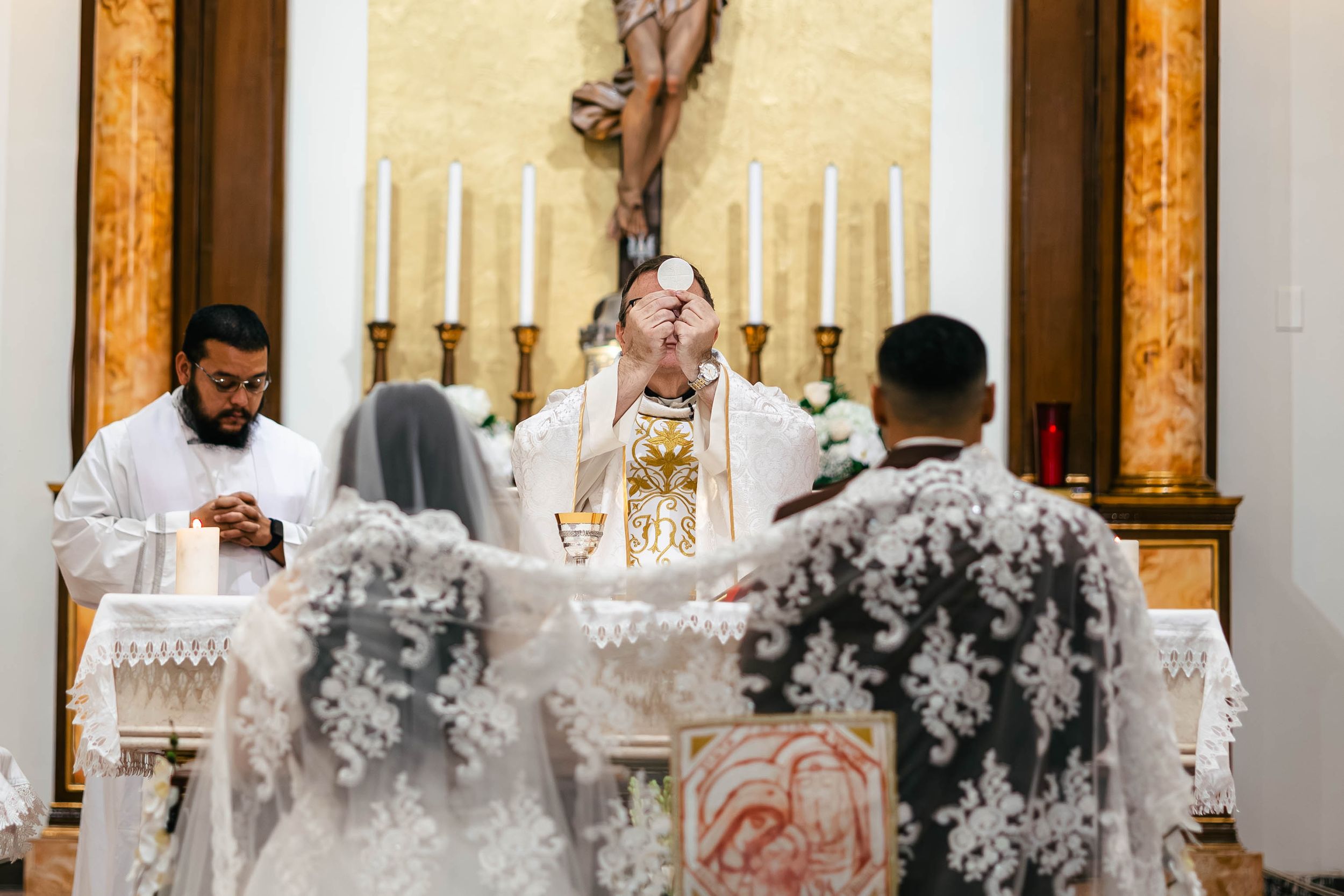 Priest officiates a Catholic wedding ceremony at the altar with candles and a crucifix in a church.