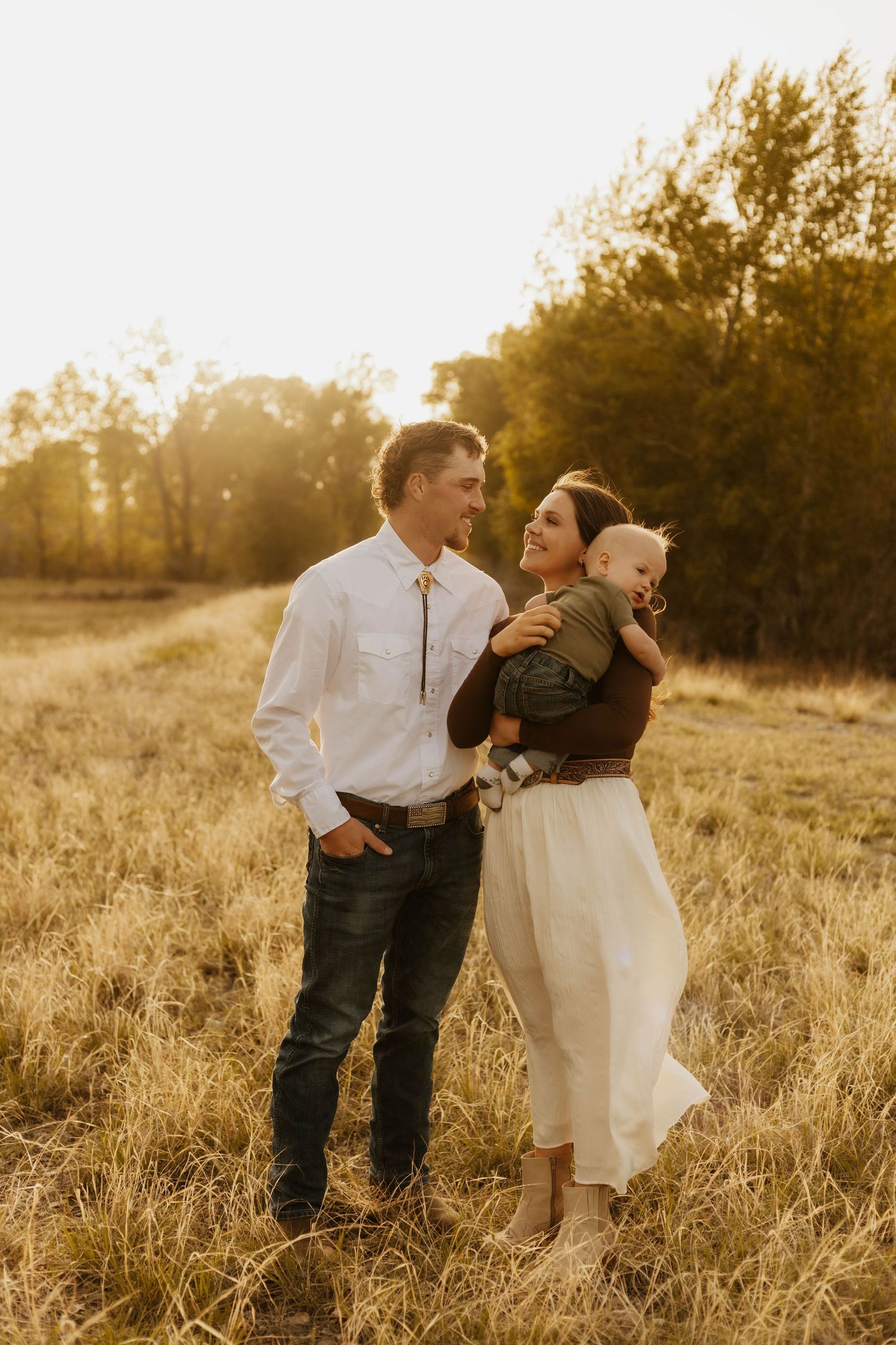 A western couple poses playfully in a sun-drenched field during golden hour.