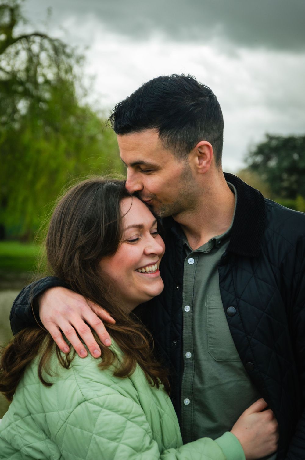 Couple sharing intimate moment outdoors with cloudy sky in background.