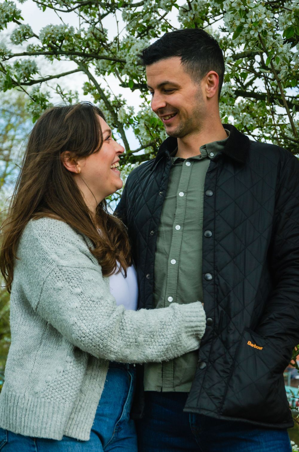 Couple embracing and laughing together under blooming spring trees.