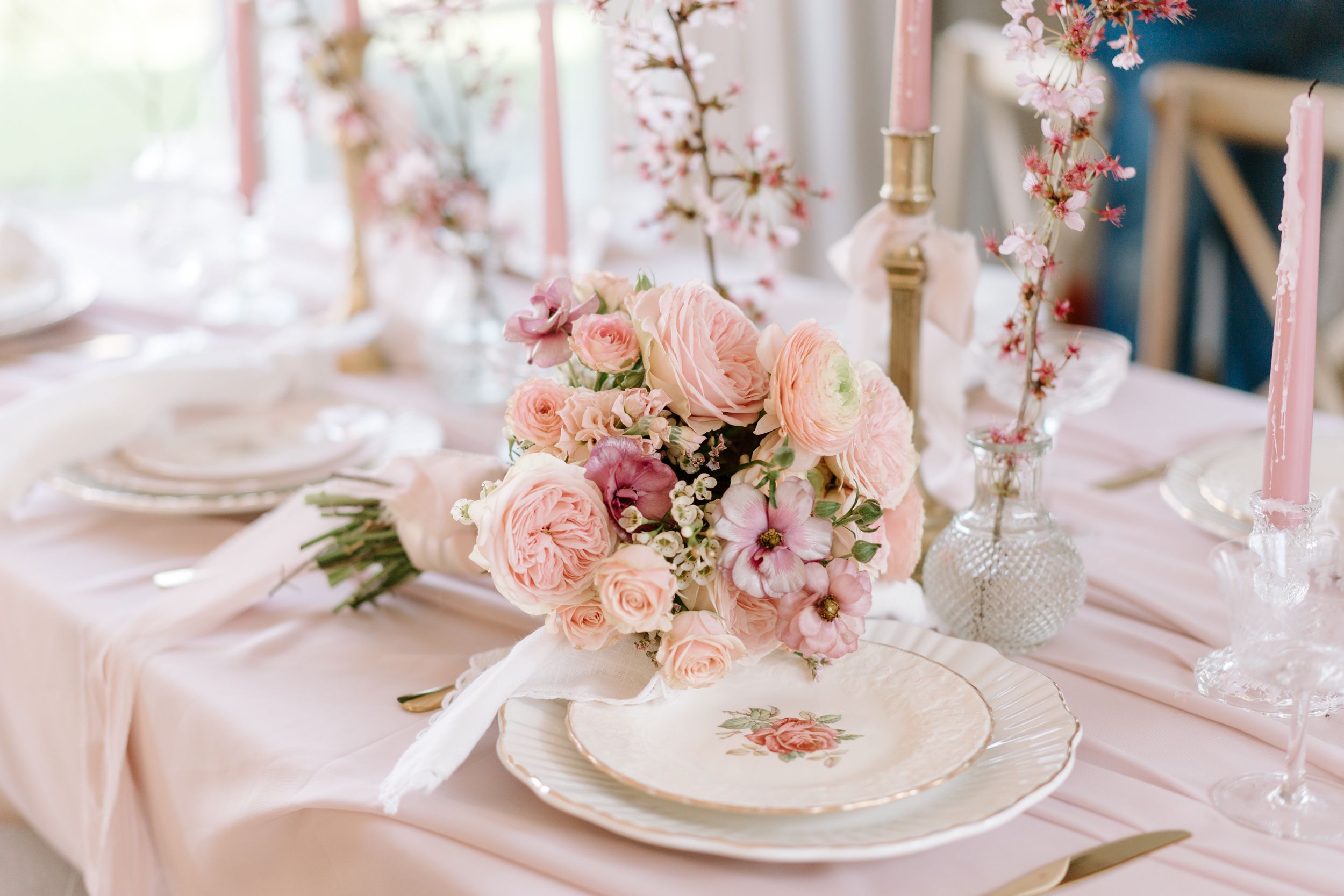 Pink floral centerpieces with roses and delicate blossoms adorn elegant table settings at a romantic wedding reception.