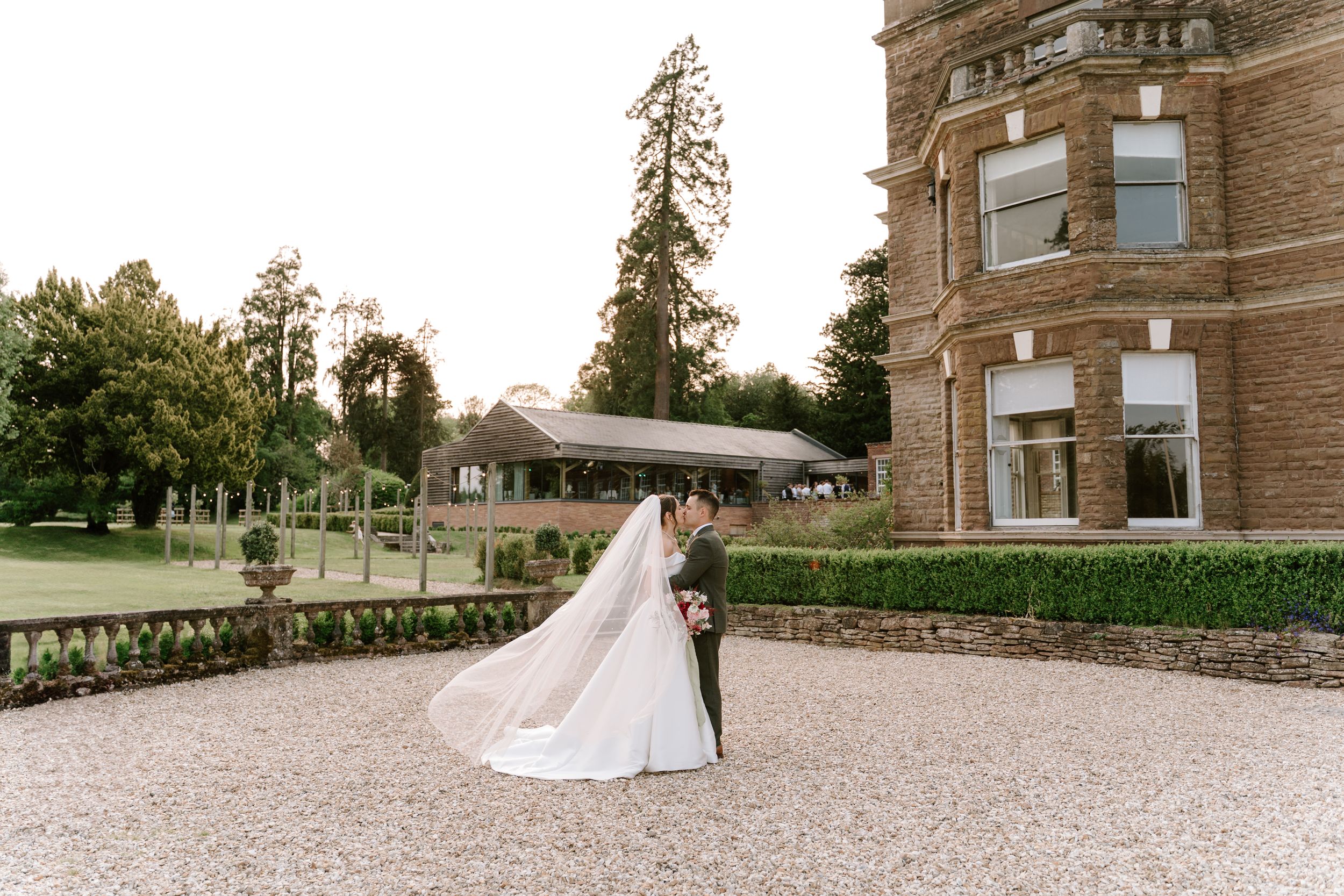A couple walks on the gravel pathway outside a grand stone manor house on their wedding day.