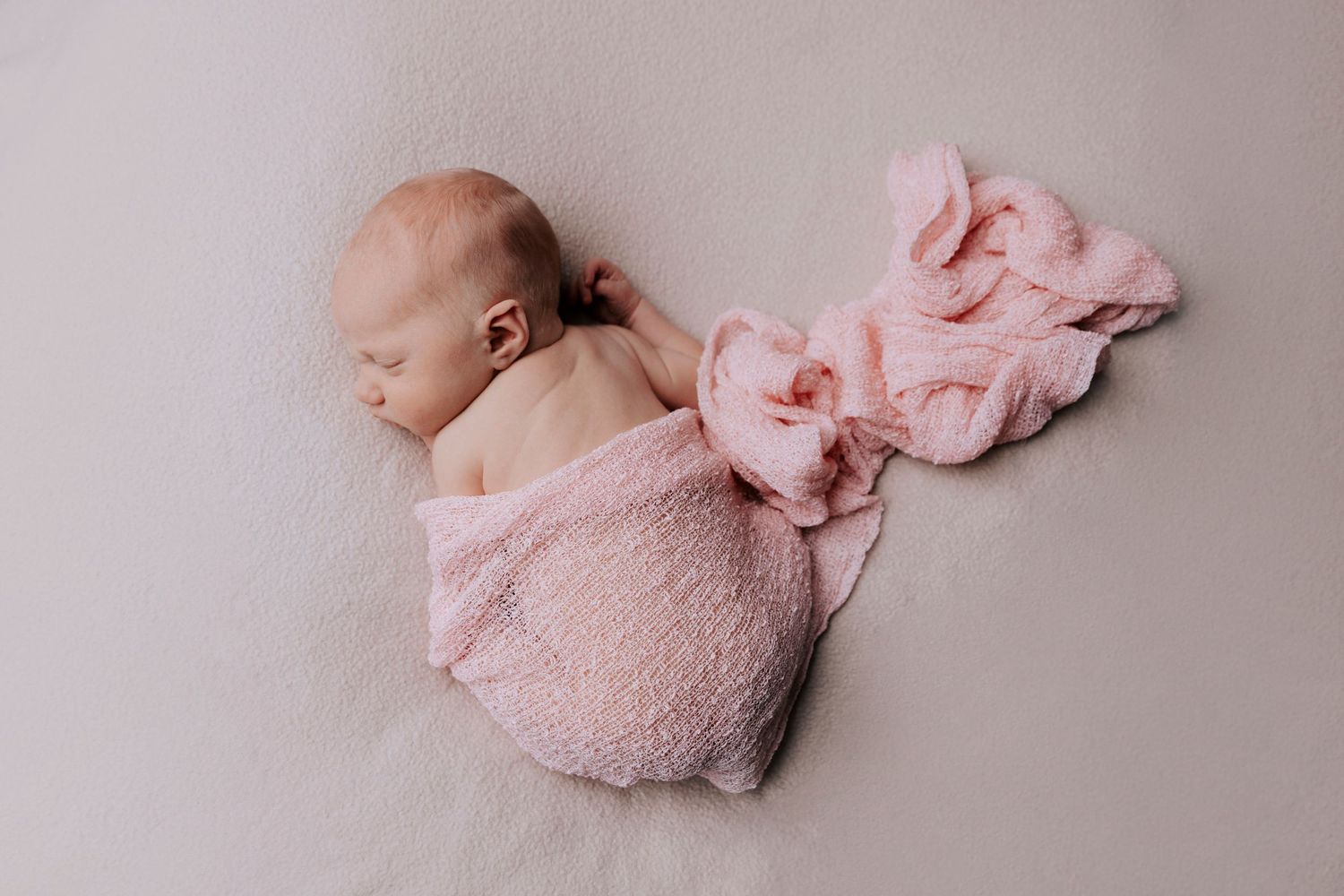 newborn baby girl sleeping on her tummy covered in a pink cheesecloth