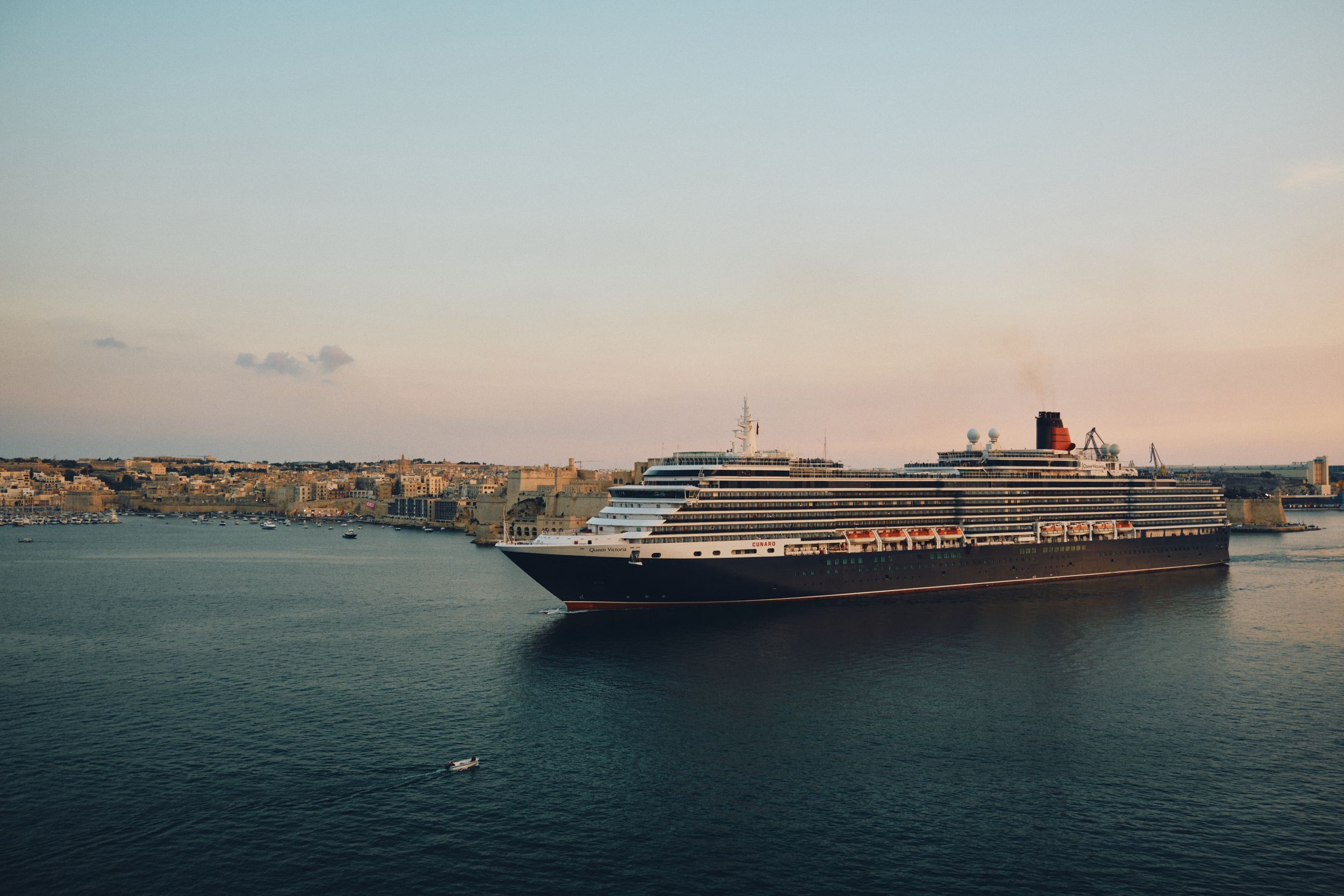 A large cruise ship docked in a Mediterranean harbor during sunset.