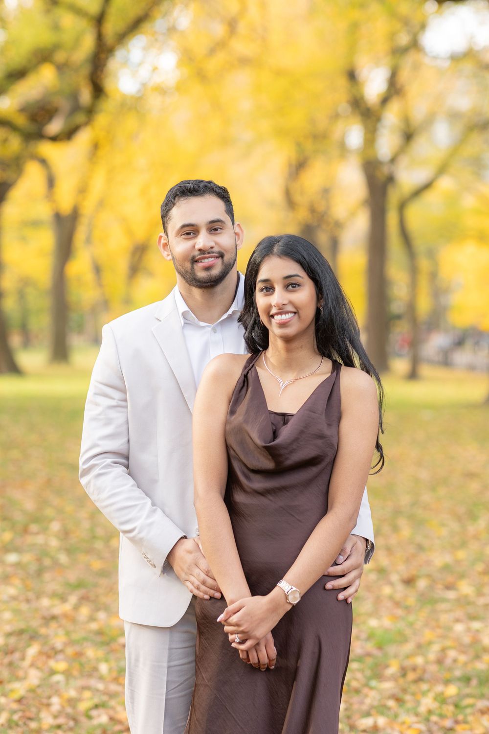 A couple poses together in a park with golden autumn foliage creating a warm romantic backdrop.