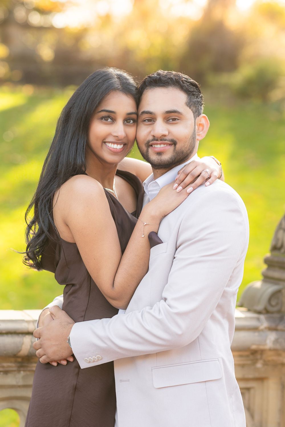 A couple embraces outdoors during golden hour in a romantic portrait against a blurred nature background.