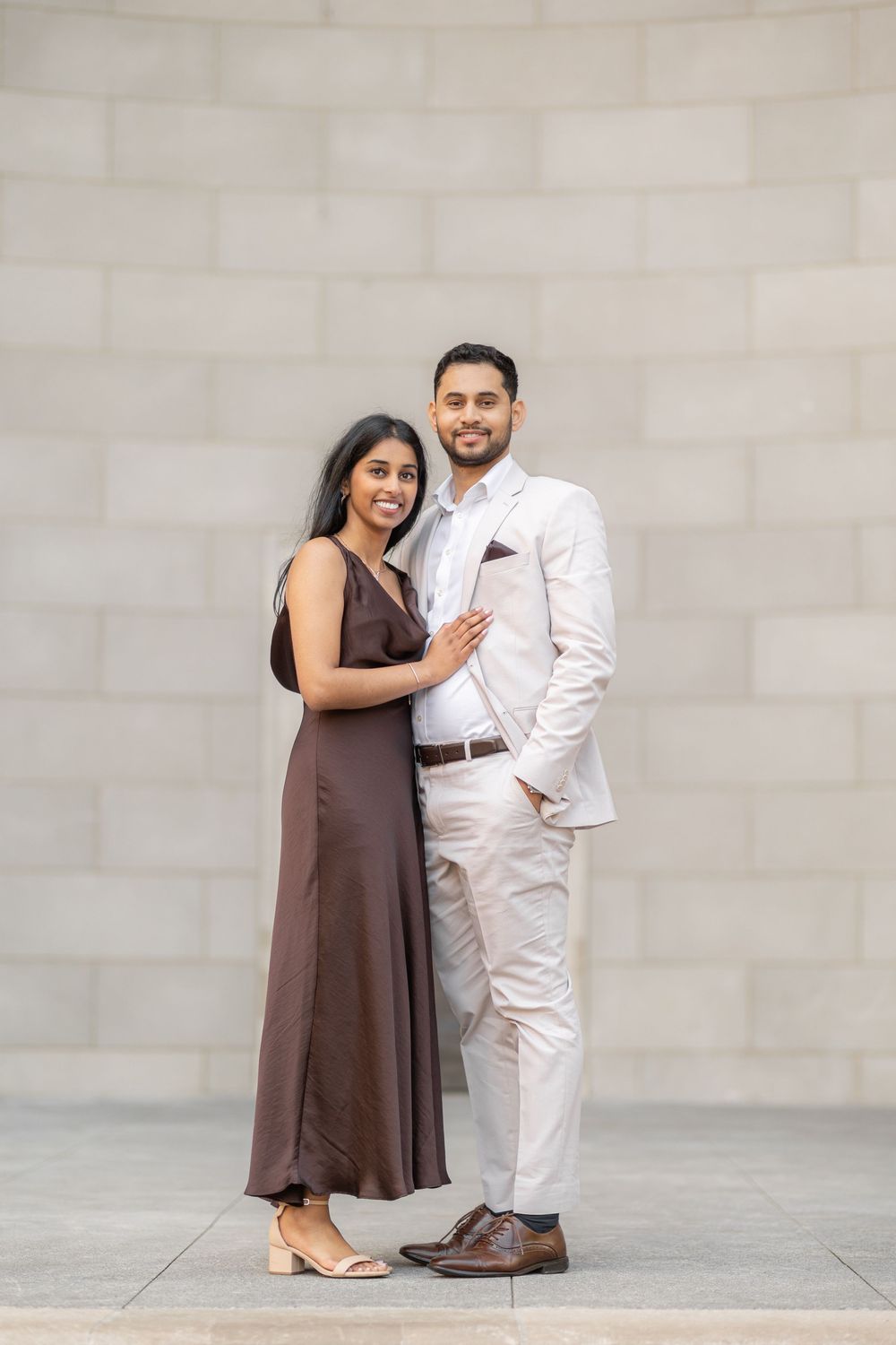 A couple poses together against a neutral wall, wearing contrasting brown and white outfits in a series of casual shots.