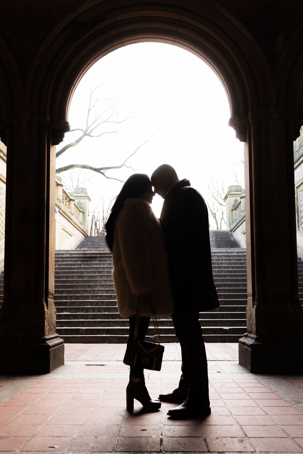 Silhouetted figures share a tender moment under an illuminated stone archway.