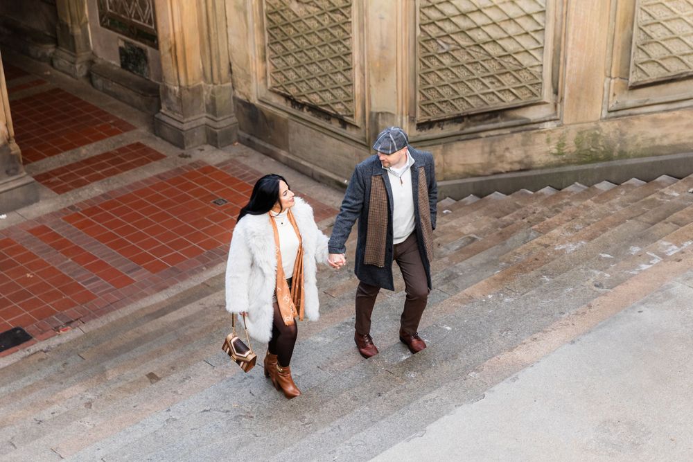 A couple walks hand in hand on brick pavement wearing coordinated winter outfits.