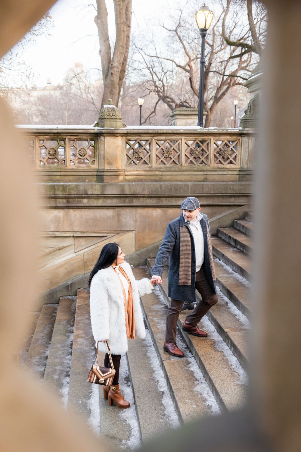 A couple ascends stone steps while holding hands, framed through architectural details.
