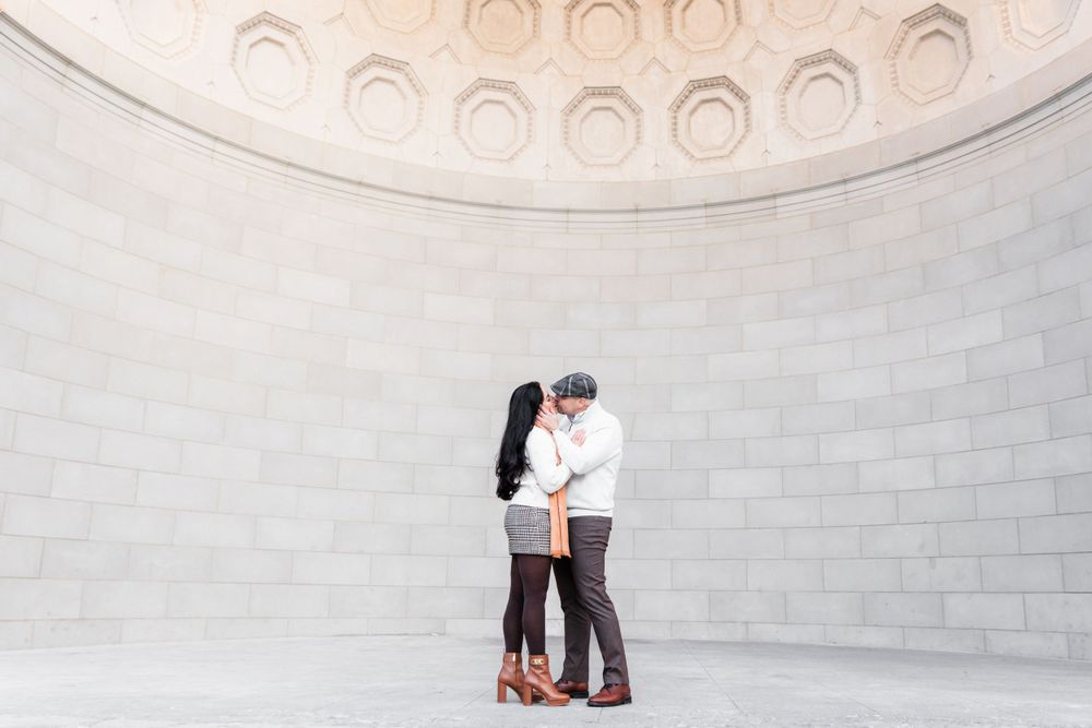 A couple embraces intimately under an ornate domed ceiling with architectural details.
