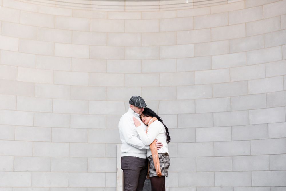 A romantic moment shared against a curved stone wall backdrop.