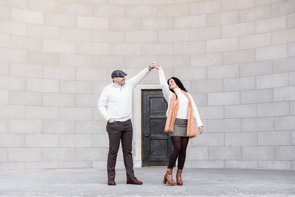 A couple dancing and twirling together against a grey stone wall with a door.