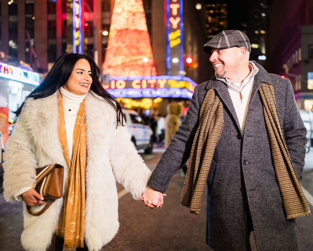 A couple walking hand in hand through city streets with bright lights and signage.