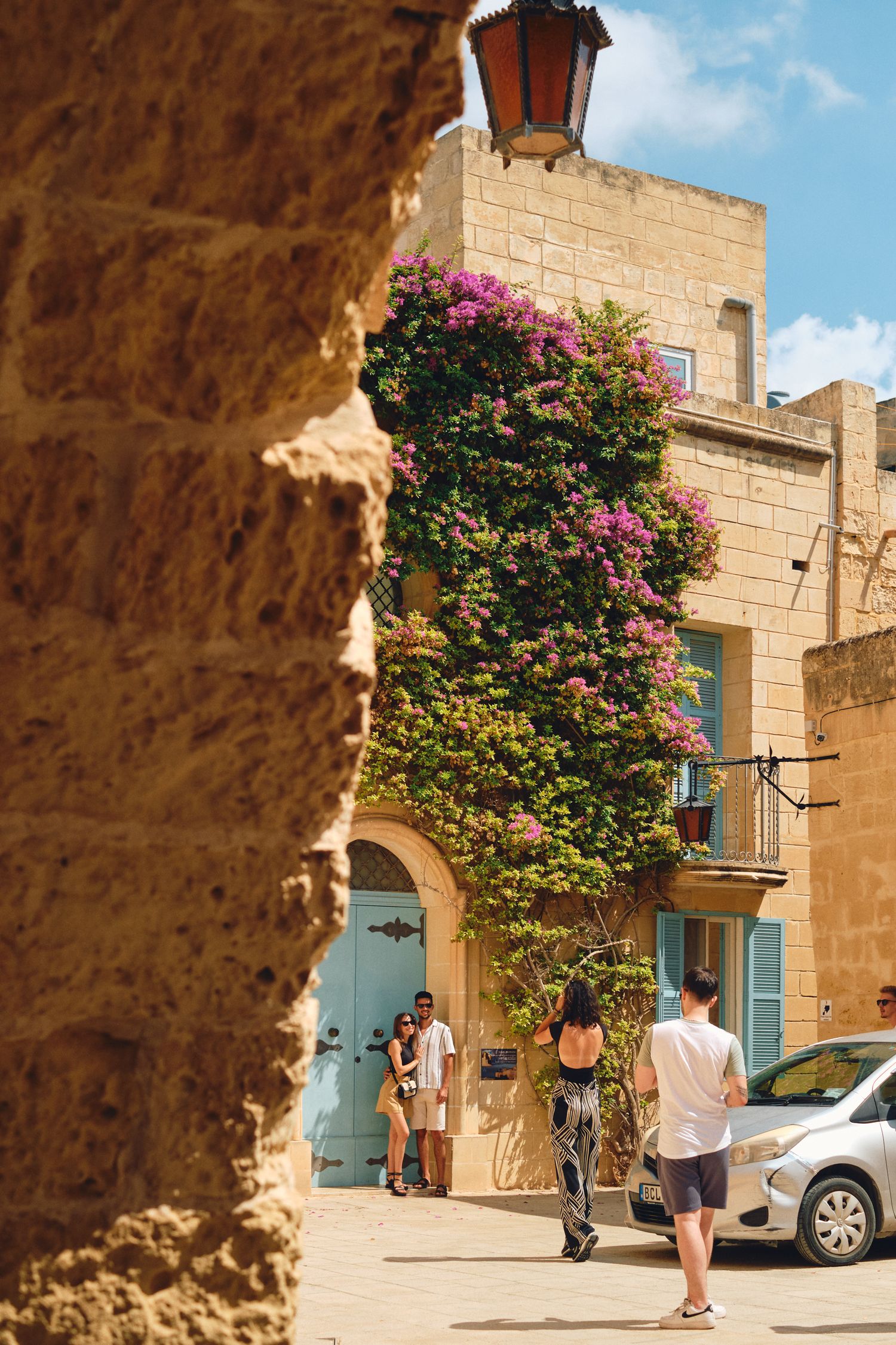 Historic Mediterranean street with vibrant bougainvillea flowers climbing up a sandstone building facade.