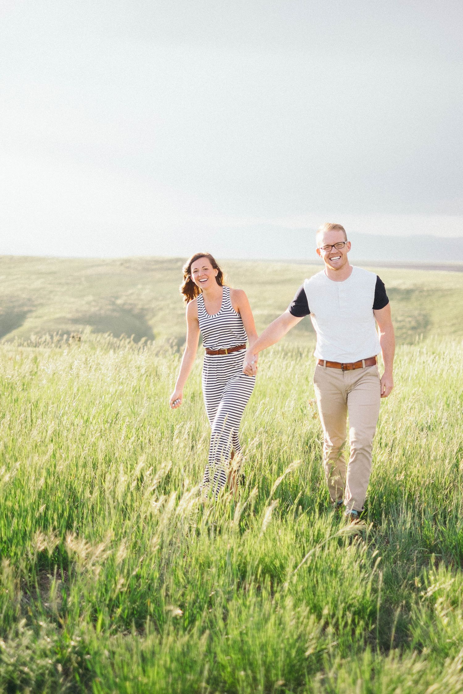 Couple walking together through tall grass in a sunny meadow landscape.