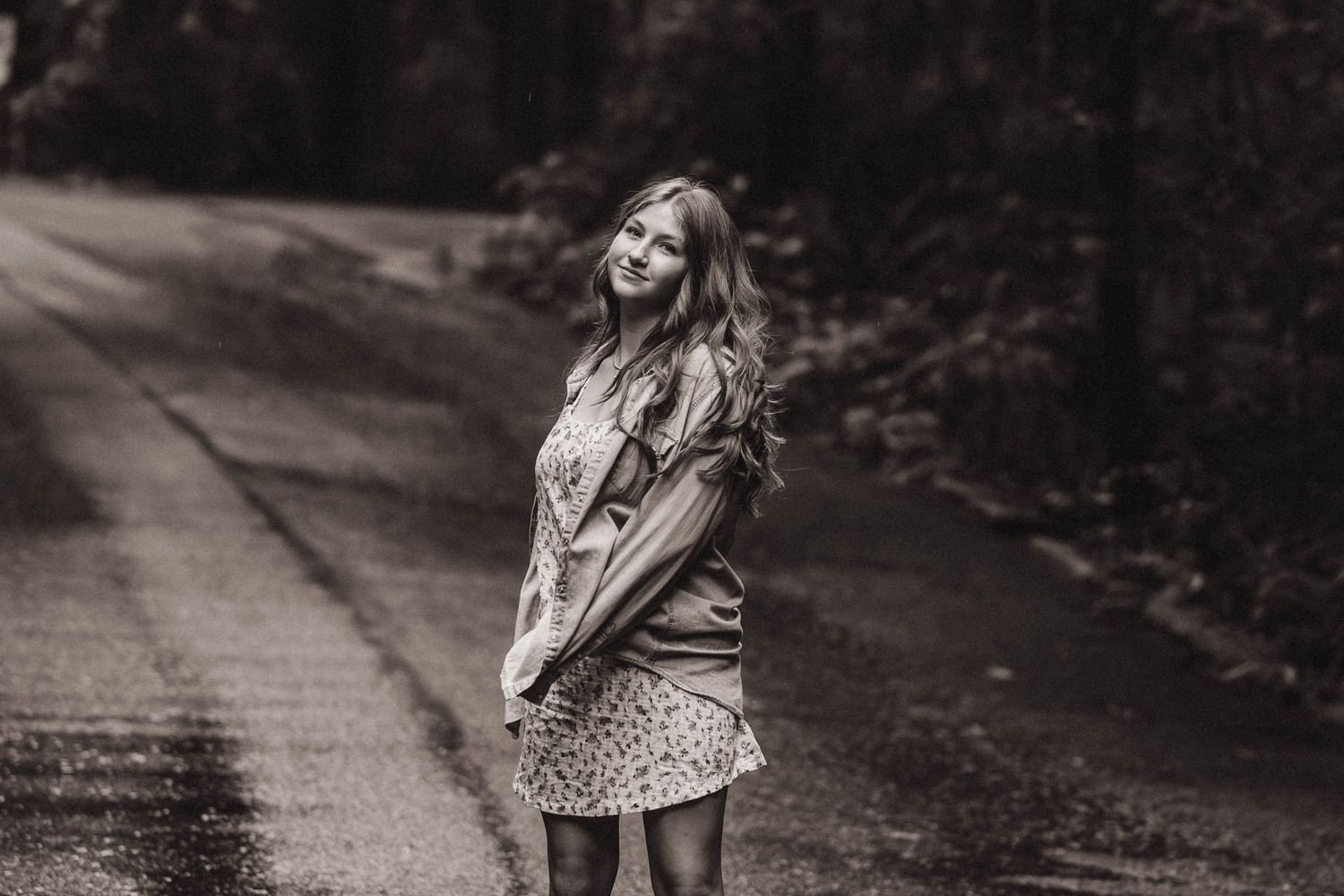 Black and white portrait of woman joyfully dancing on rural road.