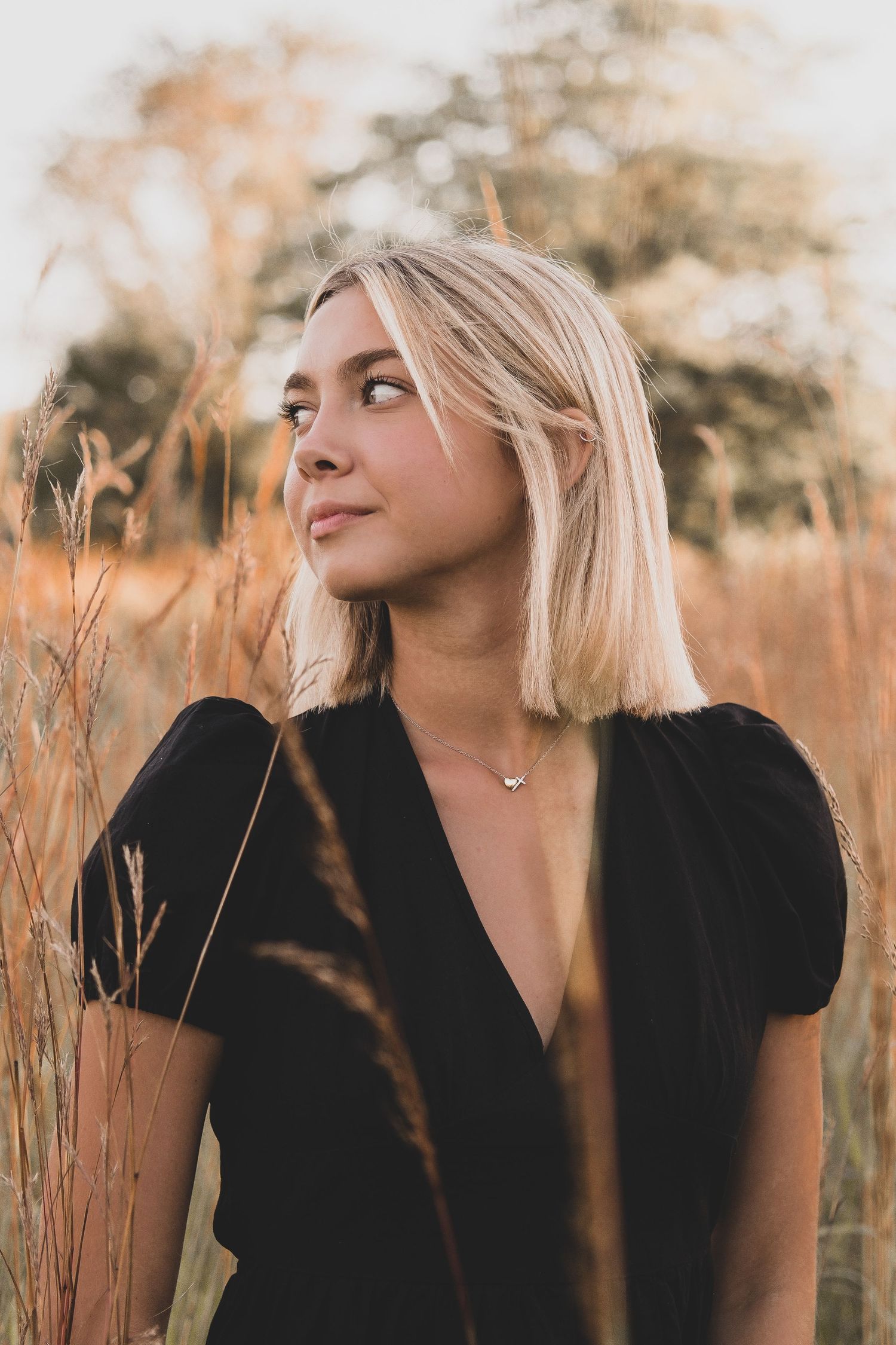 Artistic portrait in black attire against warm-toned tall grass at sunset.