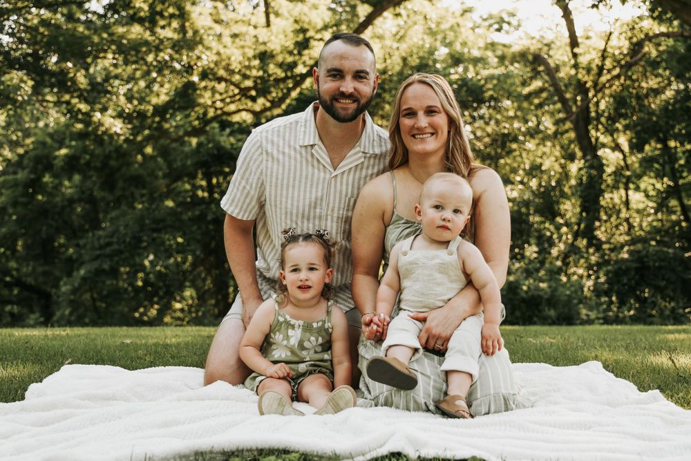Family sitting together on white blanket during outdoor summer photoshoot.
