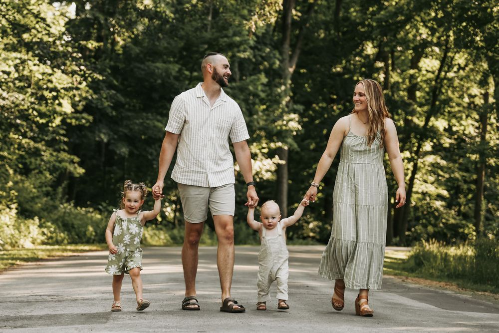 A family holds hands while walking together on a tree-lined path.