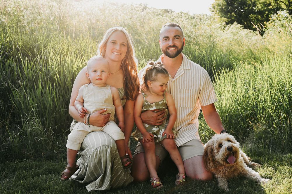 A happy family with their goldendoodle dog posing together in a sunny meadow at sunset.