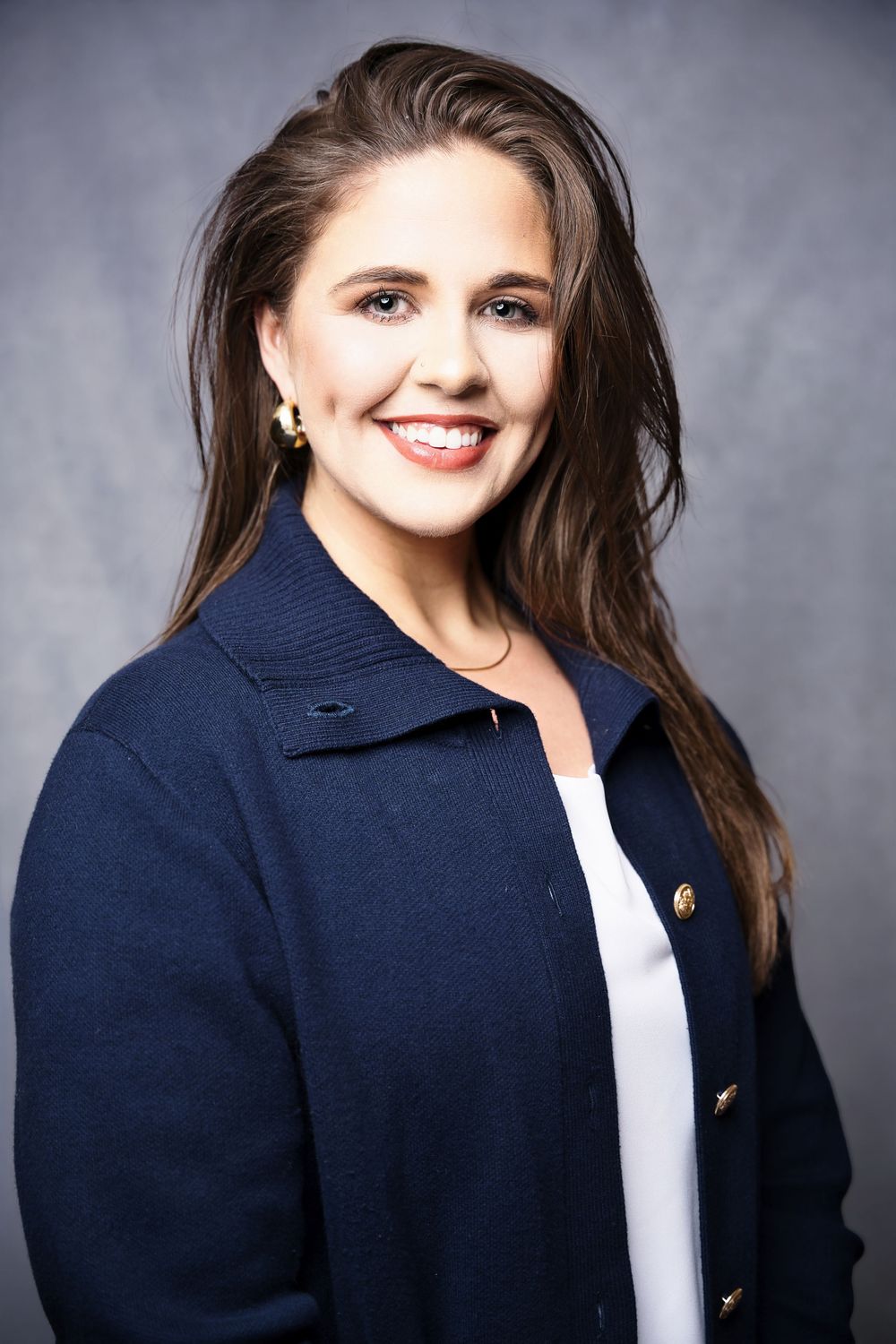 Professional headshot series showing a person in a navy blazer and white top against a gray background.