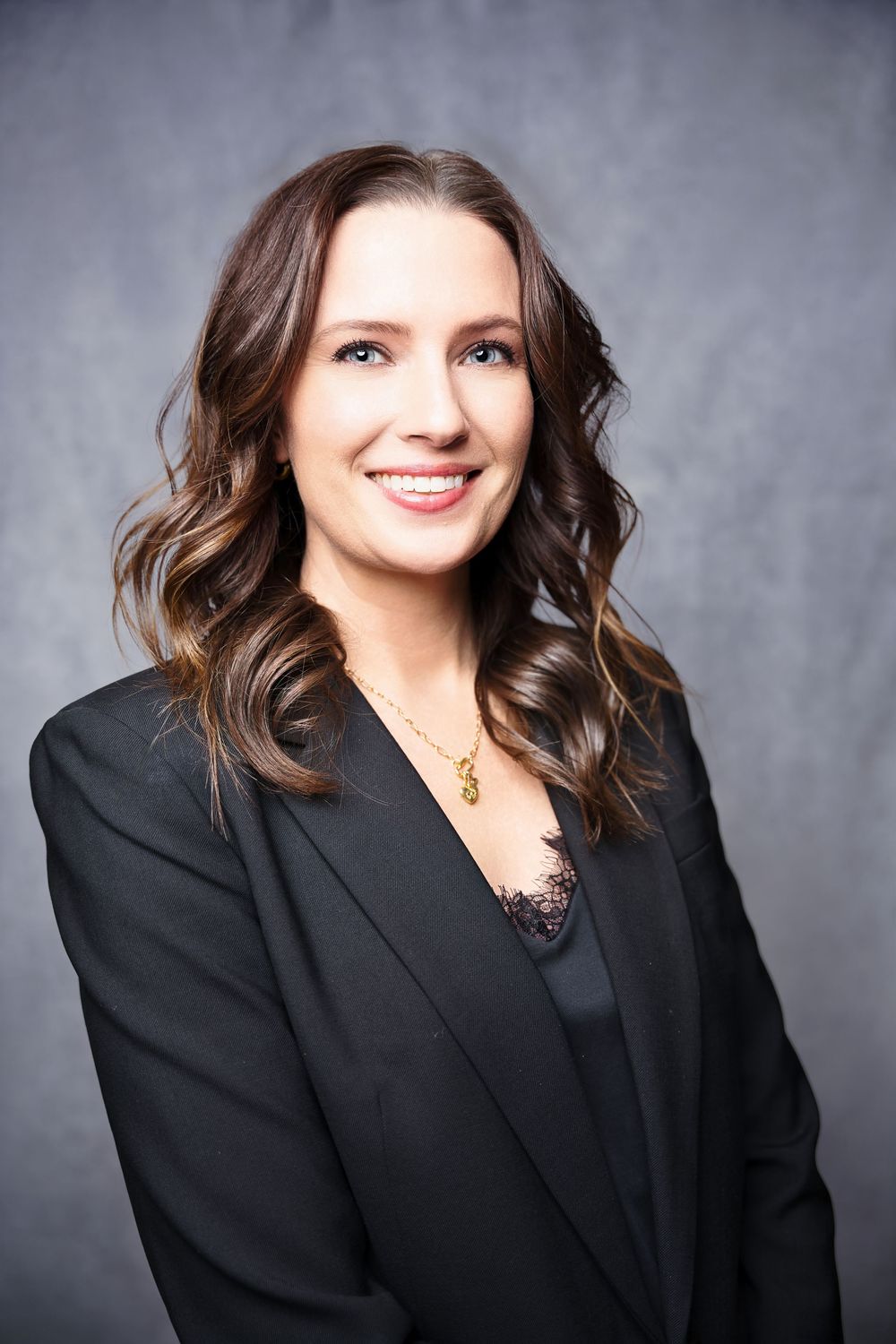 Professional headshot series showing a person in a black blazer and dark top against a gray background.