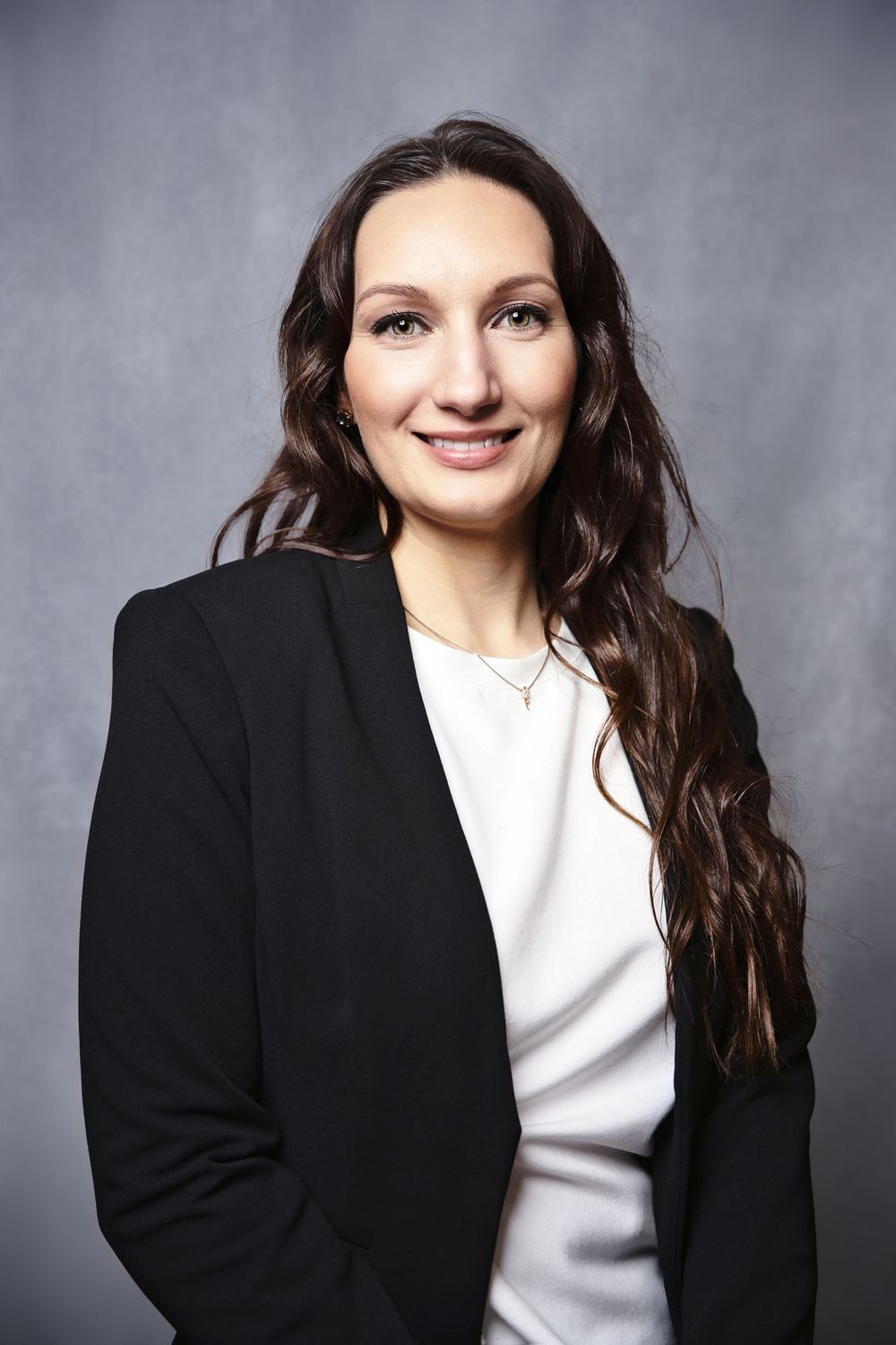 Professional portrait of a person in a black blazer and white top smiling against a gray background.