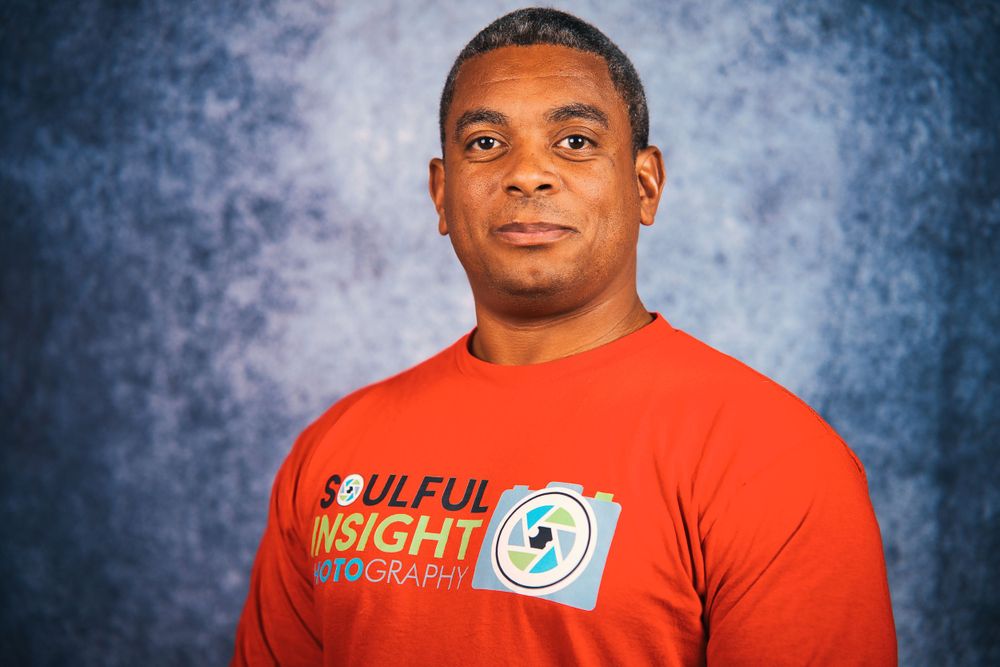 Portrait of photographer wearing red t-shirt with logo against blue background.