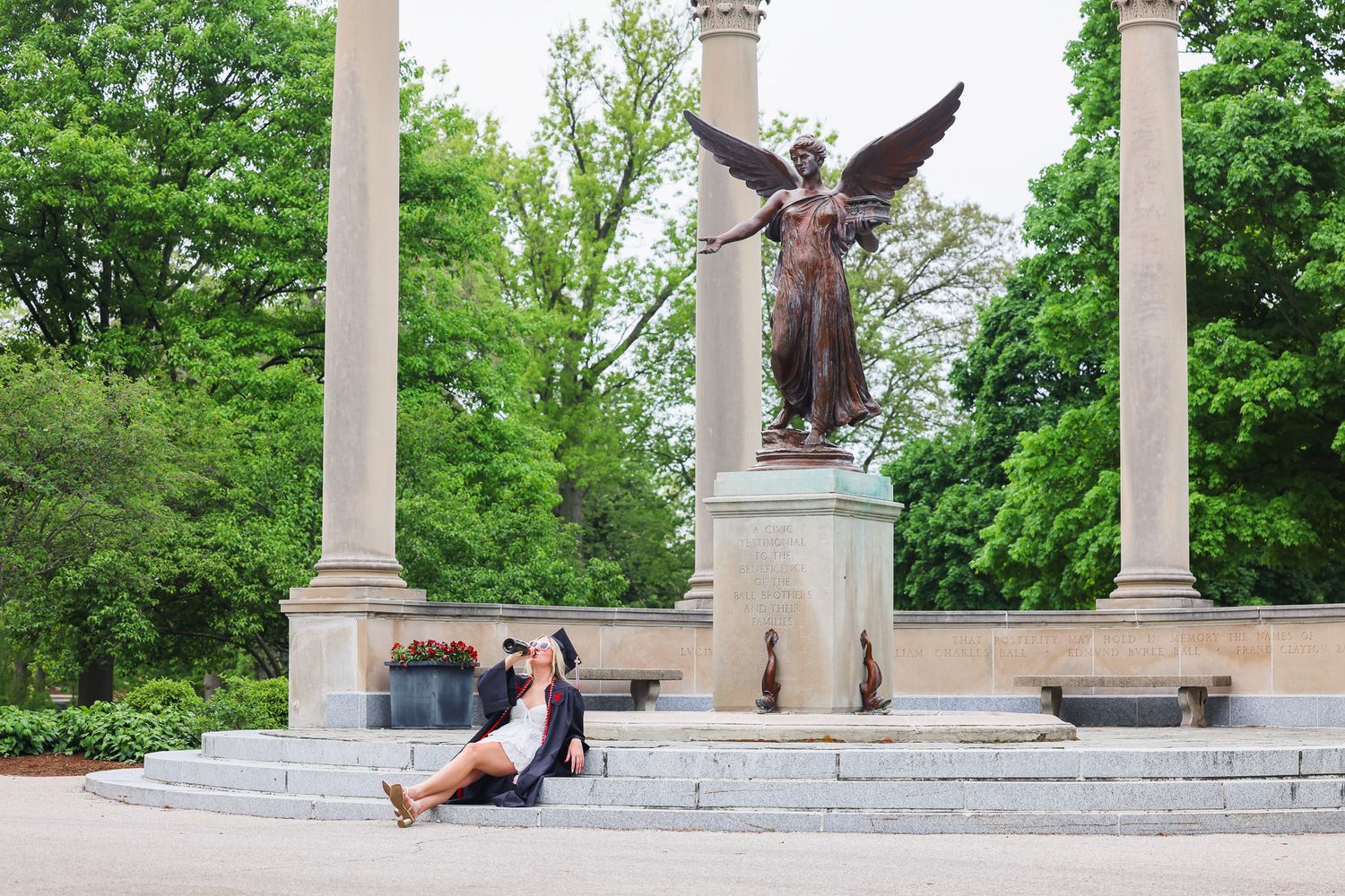 Angel statue monument in park with stone columns and greenery.